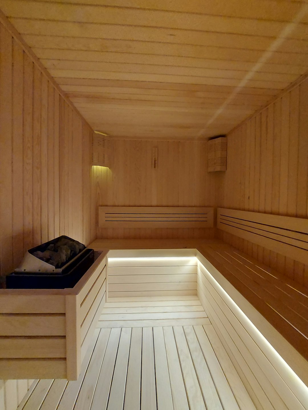 a wooden room with a bench and a light - Infrared Saunas