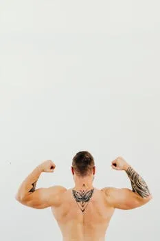 Shirtless tattooed man displaying strong muscles while flexing arms in a