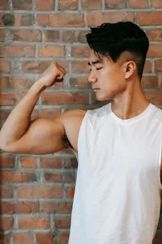 Young ethnic powerful male demonstrating strong bicep on arm near brick wall