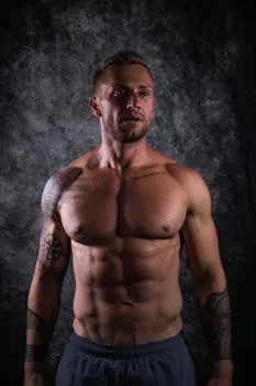 Studio portrait of a muscular man showing defined physique and tattoos.