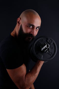 Bald man with a beard lifting a dumbbell, showcasing strength and fitness in