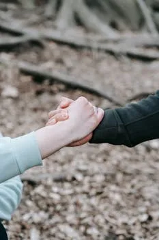 Two people holding hands in a peaceful fall forest setting, symbolizing