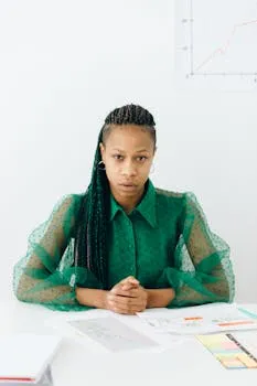 A determined businesswoman in a green blouse sits at a desk with charts and