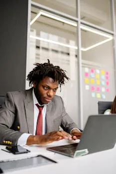 Black businessman in formal attire working intently on a laptop in a modern