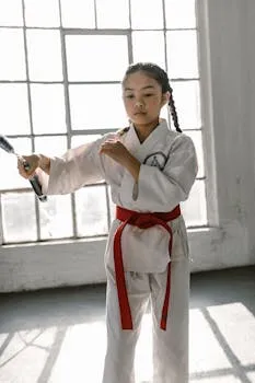 A young martial artist in a karate uniform practicing with nunchaku indoors.