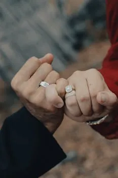 Close-up of a couple linking pinkies, showcasing wedding rings in a romantic