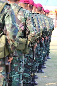 A group of soldiers in camouflage uniforms with berets line up outdoors,