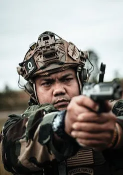 Close-up of a soldier in camouflage aiming a pistol outdoors, showcasing