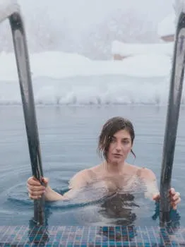 A woman enjoys a serene swim in an outdoor pool during a snowy winter day.