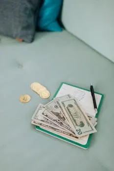 A close-up of US dollar bills and cryptocurrency coins on a notebook with a pen.