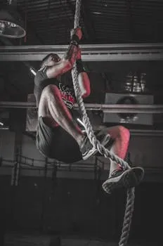 A determined man climbing a rope in an indoor gym setting, showcasing