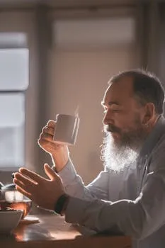 Elderly man holds a steaming cup of coffee in a warm, indoor setting during