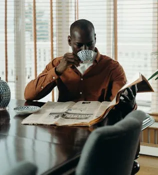 African American man enjoying coffee while reading newspaper indoors, in a