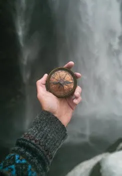 Person with compass near waterfall — discipline as identity and direction