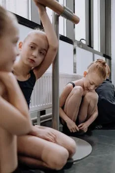 Young ballerinas in leotards resting during ballet practice in a dance studio.