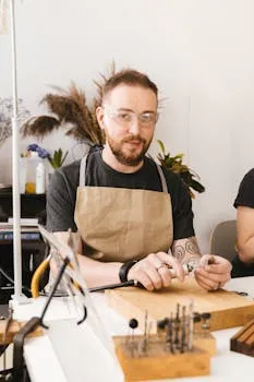 Tattooed craftsman wearing apron and goggles working on tools at a workshop