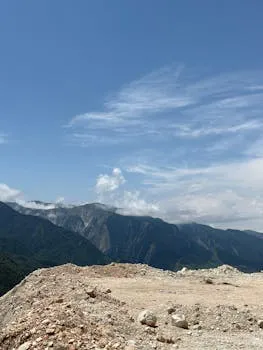 Vast mountain range under a bright summer sky with rolling green valleys below.