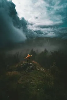 Lone hiker on a foggy summit with dramatic stormclouds rolling in behind.