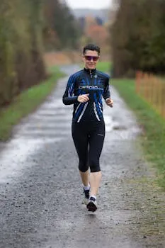 Adult woman running on a wet, forested path in outdoor sportswear,