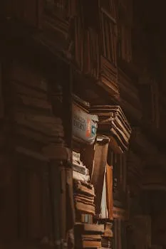 A dark moody photo of stacked vintage books on a bookshelf casting shadows.