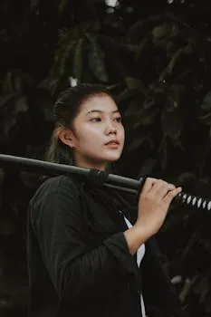 A portrait of an Asian woman holding a katana, set against a natural backdrop.