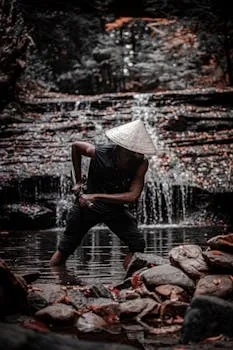 A samurai figure in traditional attire stands by a waterfall, embodying