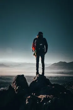 A lone hiker stands on a rocky peak, overlooking breathtaking mountains at