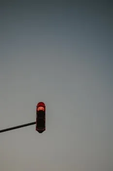 A red traffic light shines against a clear blue sky, with a minimalistic