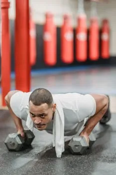 Concentrated muscular sportsman performing push ups on dumbbells in modern