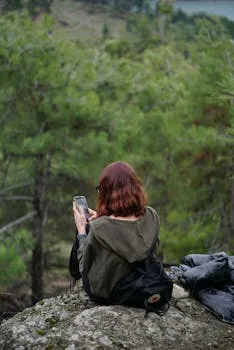 A woman sits on a rock in a forest, using her smartphone amid lush green