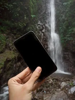 Crop anonymous traveler with cellphone standing near river falling from