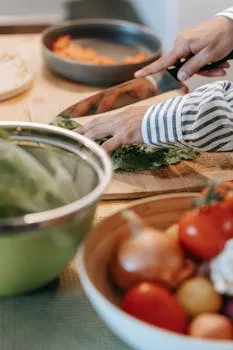 A person slicing fresh greens on a wooden cutting board in a modern kitchen