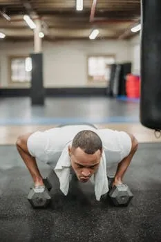 Strong ethnic sportsman in activewear doing pushups with dumbbells in modern