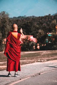 A monk in traditional attire stands outdoors, capturing the serene mountain