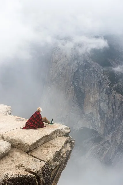 Man standing alone on cliff edge overlooking misty valley representing