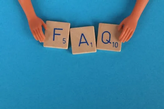 Flat lay of scrabble tiles spelling FAQ with toy hands on a blue background,