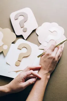 Photo of paper question marks with hands and a pen suggesting curiosity and