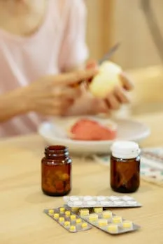 Crop anonymous female peeling apple at table with jars filled with pills at home