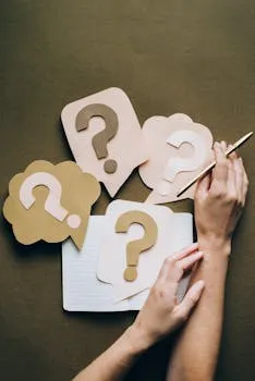 Hands holding pen next to paper question marks on notebook, symbolizing
