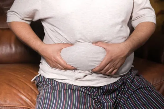 A close-up view of a man holding his tummy while sitting on a couch,