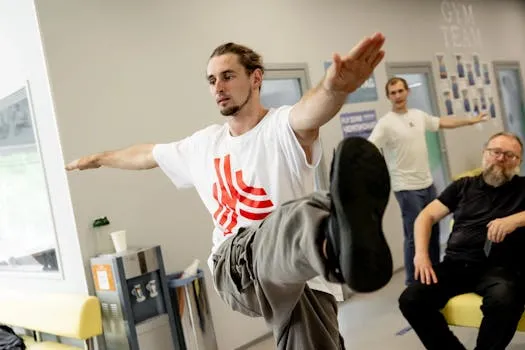 A man performs a balancing exercise in a room with two others watching.
