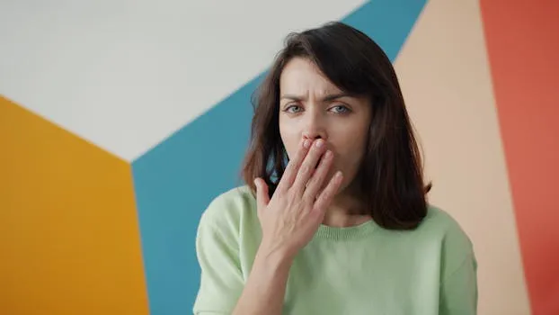 Woman covers her mouth against a colorful geometric wall, expressing