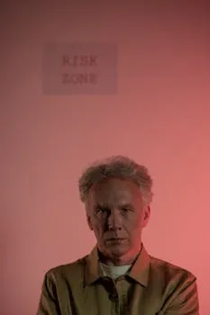 Elderly man with gray hair in risk zone, red lighting, looking serious.