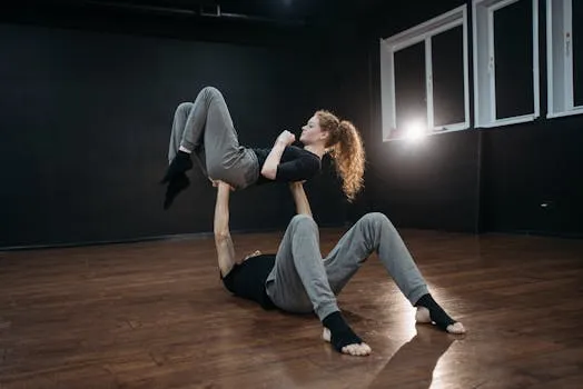 Two dancers performing acrobatic lift on a wooden floor in a studio.