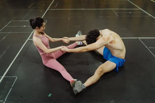 A man and woman performing partner stretching exercises on a gym floor,