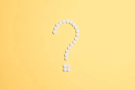 White pills arranged into a question mark shape on a vibrant yellow background.